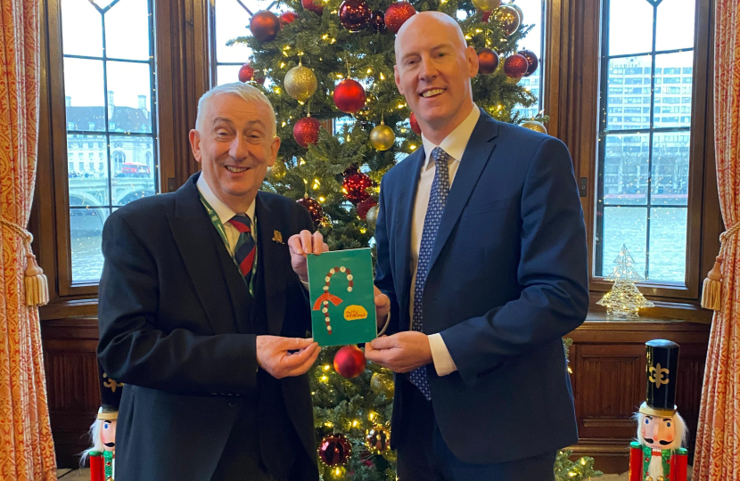 Kieran and Speaker Sir Lindsay Hall holding winning Christmas card in front of Christmas tree in Speakers House