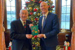 Kieran and Speaker Sir Lindsay Hall holding winning Christmas card in front of Christmas tree in Speakers House