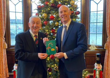 Kieran and Speaker Sir Lindsay Hall holding winning Christmas card in front of Christmas tree in Speakers House